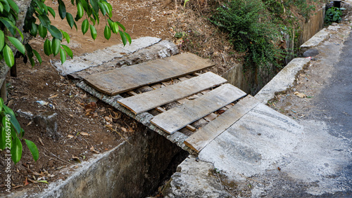 Foto Small wooden plank bridge crossing over a concrete roadside drainage ditch to connect a road and slope