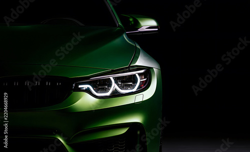 Luxury green sports car front close up with illuminated LED headlight, detailed grille and dramatic lighting against a dark background, automotive design concept.