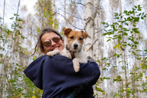 Woman holding small terrier puppy beside leafy city wall