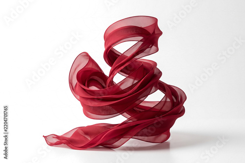 Gracefully swirling vibrant crimson fabric creating an elegant and dynamic abstract form against a pristine white background, showcasing intricate drapery and soft textures in a modern studio setting