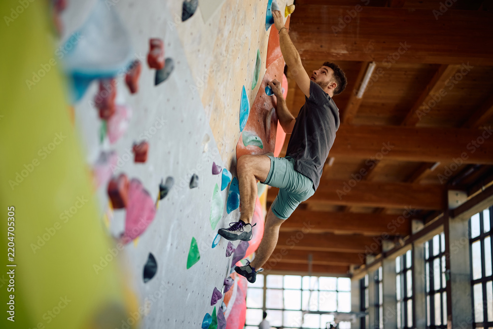 Obraz premium Below view of athlete practicing climbing technique on bouldering wall.