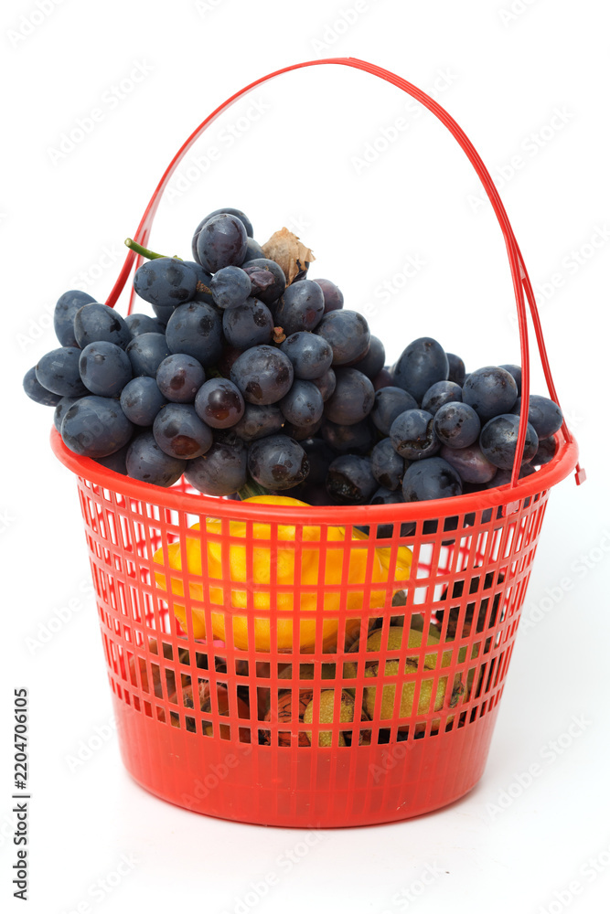 Obraz premium Red basket holds dark grapes and yellow lemons. Fresh fruit displayed in simple, vibrant container. Bright red basket contrasts with white background