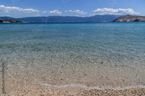 Crystal clear turquoise shallows over pebbles at Baška beach with the Velebit mountains across the channel, Krk island, Croatia