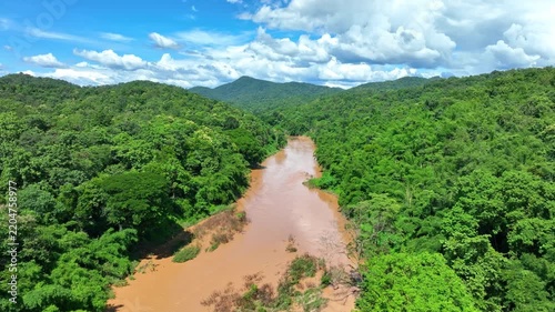Aerial view shows a flooded tropical river surrounded by dense green forest, emphasizing climate extremes, intense rainfall, rising flood hazards and ecosystem resilience. Phrae, Thailand. 4k.
