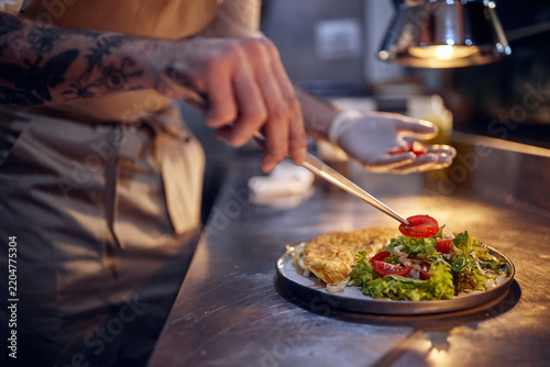 Close up of chefs hand decorating meal. Cook in Professional Modern  kitchen, restaurant concept
