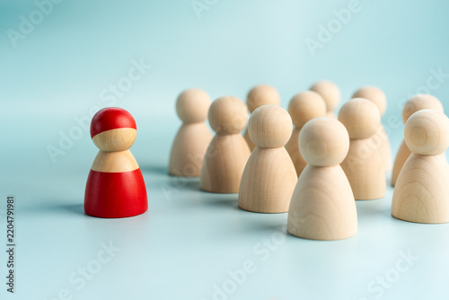 Leadership and individuality concept, red wooden peg doll leading group of natural wood figures on blue background, symbolizing business management, standout talent, and team guidance.