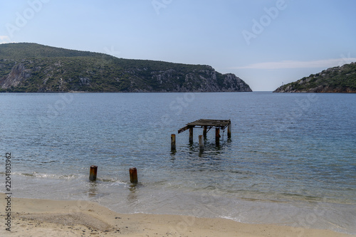 Porto Koufo natural harbour on a hazy sunny day with ruined jetty posts in the water and the rocky bay entrance, Sithonia, Chalkidiki, Greece