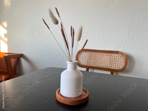 Simple white ceramic vase holding dried decorative grass, placed on a dark table in a cozy minimalist room.