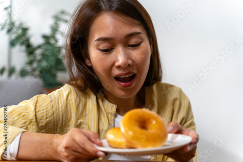 Woman holding up a plate of glazed doughnuts with mouth open