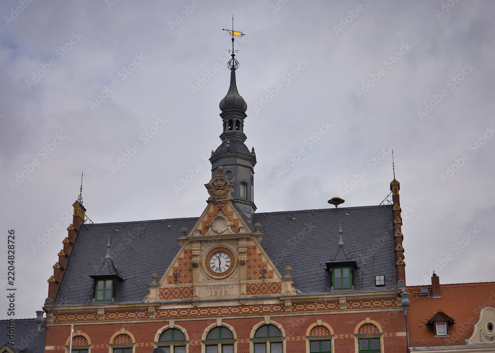 Obraz premium Historisches Rathaus und angrenzende Gebäude am Marktplatz von Dahlen mit parkenden Autos vor bewölktem Himmel – Landkreis Nordsachsen, Sachsen, Deutschland