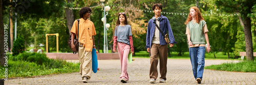 Website header shot of multiethnic diverse teenagers walking together in park holding skateboards, enjoying youth friendship outdoors. Ideal for youth lifestyle marketing and back to school campaigns