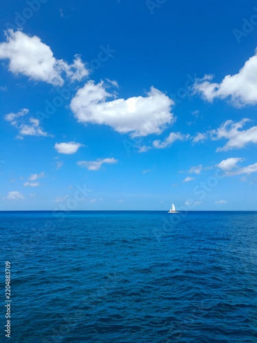 Beautiful minimalist ocean landscape with lone sailboat on horizon under blue sky with fluffy white clouds — perfect background for summer travel advertising, tourism marketing, and nature concepts