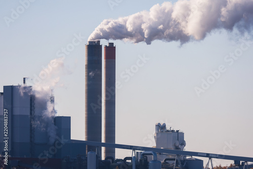 An industrial plant with tall, smoking chimneys set against a clear sky, symbolizing manufacturing, energy production, or environmental pollution