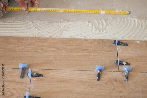 Worker installing floor tiles with leveling system and measuring tape