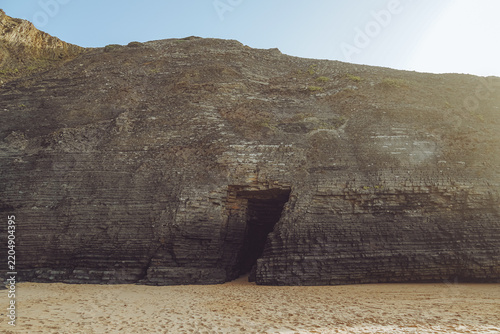 Stunning dark cave opening on the sandy shores of Praia da Bordeira, Portugal