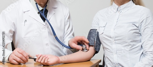 Fotografie Doctor measuring patient's blood pressure with stethoscope during checkup