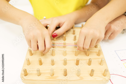 Foto Child stretches colored rubber bands around wooden pegs to recreate a geometric pattern on a geoboard during a guided educational activity