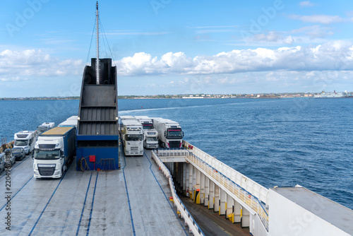 Rows of freight trucks, trailers, camper and passenger vehicles secured on the open vehicle deck of a roll-on roll-off ferry during a sea crossing. Commercial transport scene represents road freight, 