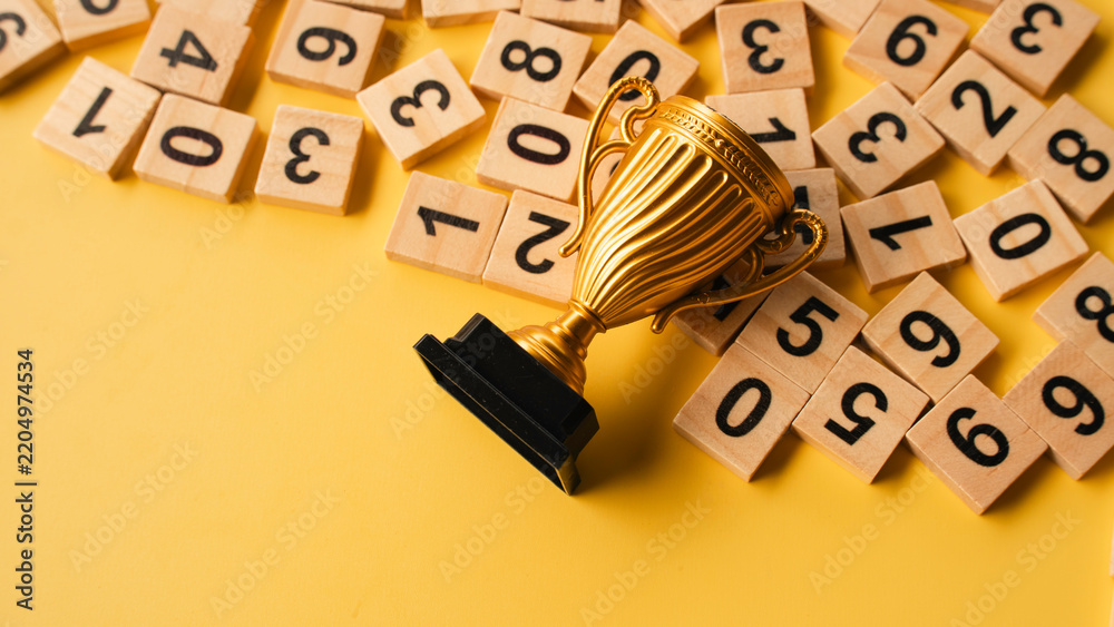 Obraz premium Golden trophy cup on wooden number tiles over yellow background representing achievement and excellence in mathematics