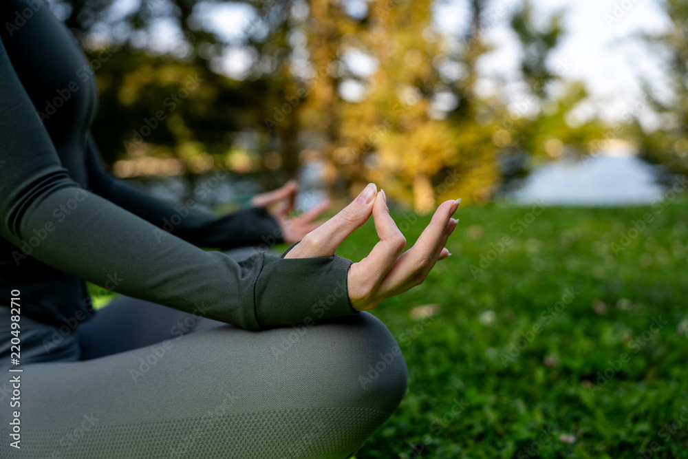 Obraz premium Woman sitting in lotus position on fitness mat practicing yoga and meditation with hand in gyan mudra outdoors on green grass in park.