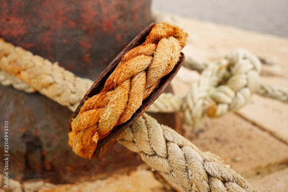 Obraz premium Heavy-duty mooring rope with a rusty metal thimble hitched on a harbor bollard. Port infrastructure and maritime concept.