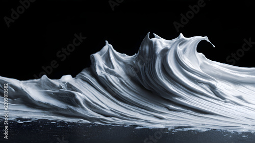 Silver shaving foam forming wave like swirls against black background, creating dramatic abstract macro texture with flowing ridges and contrast