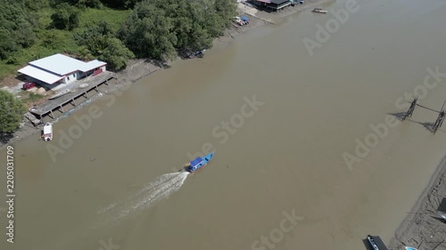 Aerial view of a riverine village with stilt houses and small boats navigating the muddy waters in Sarawak, Malaysia.