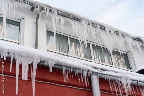 Photo of multiple icicles formed on the house. Big sharp dangerous icicles on the roof. Winter weather conditions and icicle danger in cities concept.