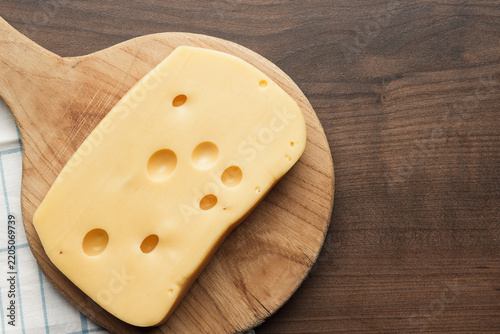 Top view of big piece of cheese on wooden cutting board with copy space.