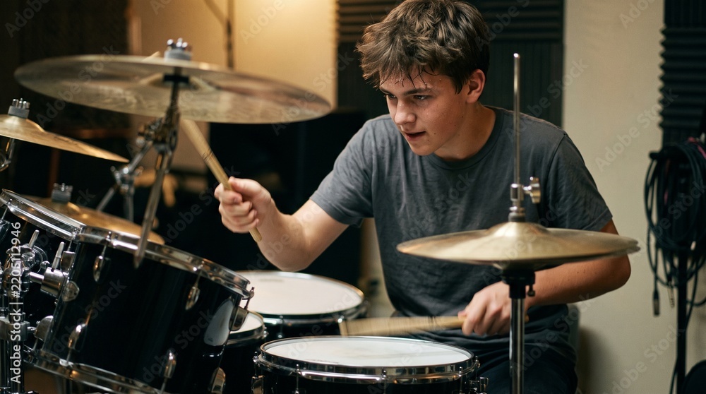 Fototapeta premium Young male drummer intensely playing drum set in a music studio with soundproofing