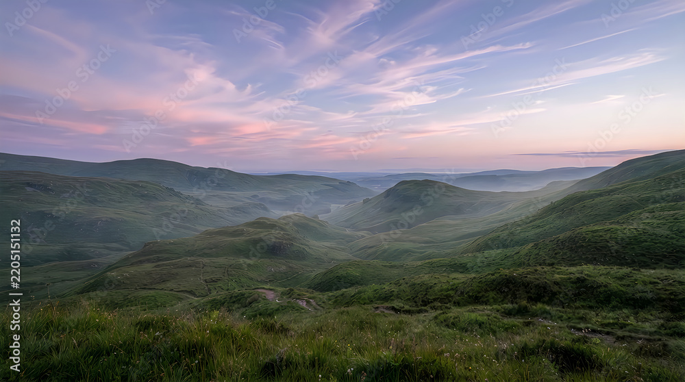 Obraz premium Breathtaking panoramic view of green rolling hills during a serene sunrise with soft colorful clouds in the sky