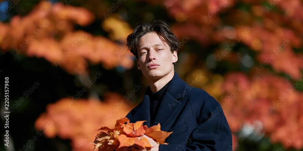 Obraz premium Autumn male portrait holding orange leaves for seasonal banner and fall background design with moody fashion styling
