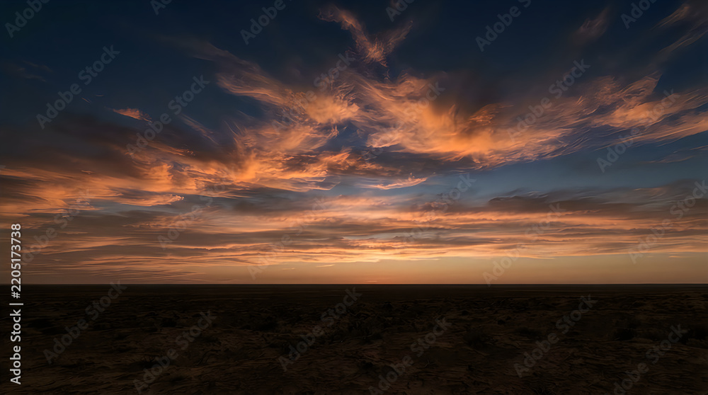 Obraz premium Vibrant orange sunset sky over a dark desert horizon landscape during the golden hour of the late evening