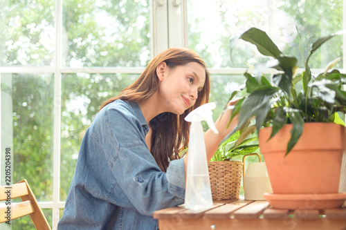 Young Asian woman caring for indoor houseplants by watering potted plants in a bright modern home