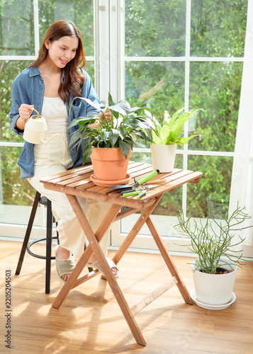 Young Asian woman caring for indoor houseplants by watering potted plants in a bright modern home