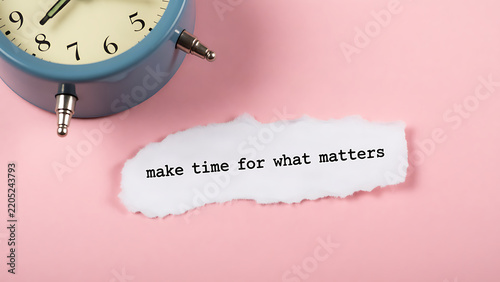Vintage alarm clock beside torn paper note reading make time for what matters on pink background