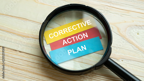Magnifying glass examining a corrective action plan on a wooden desk