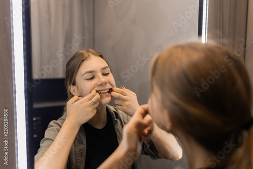 Teenage girl examining her teeth and lips in bathroom mirror, self care concept