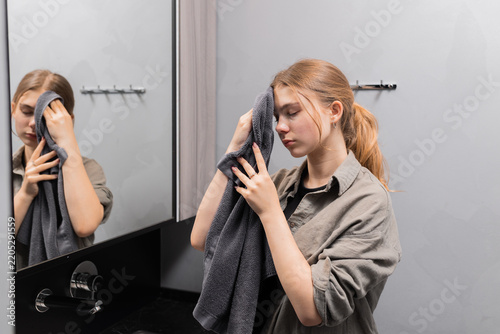 Young girl wiping her face with a soft towel while checking her reflection in mirror