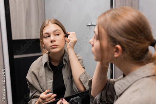 Teen girl doing her makeup while looking in mirror, beauty routine