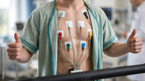 Male patient with multicolored ECG electrodes on chest gives thumbs up during cardiac stress test