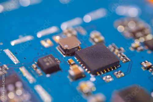 Blue circuit board with integrated chips, soldered electronic components, metallic contacts, and shallow depth of field in a macro technology detail