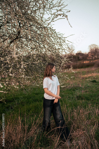 Happy teenage girl in a white T-shirt posing beside a blooming tree, retro film photo with visible grain and noise