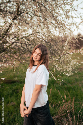 Happy teenage girl in a white T-shirt posing beside a blooming tree, retro film photo with visible grain and noise