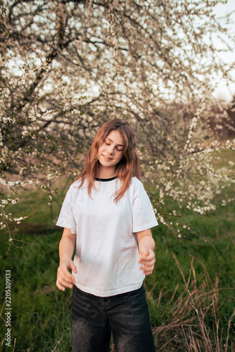 Happy teenage girl in a white T-shirt posing beside a blooming tree, retro film photo with visible grain and noise