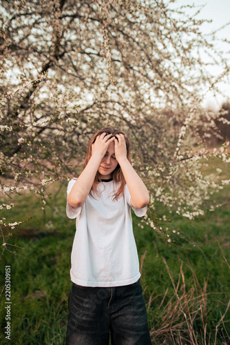 Happy teenage girl in a white T-shirt posing beside a blooming tree, retro film photo with visible grain and noise