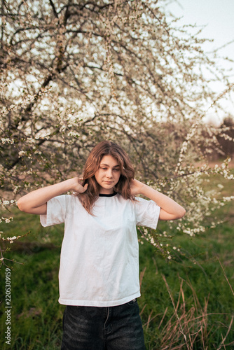Happy teenage girl in a white T-shirt posing beside a blooming tree, retro film photo with visible grain and noise