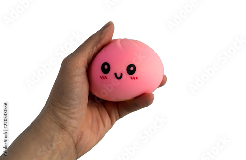 Hand squeezing a pink squishy toy with a cute kawaii face, isolated on white background. Stress relief ball, antistress sensory fidget