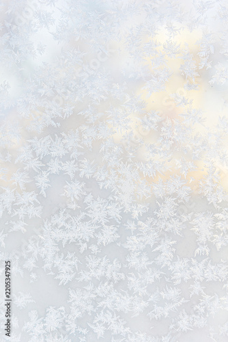 Frosty window glass texture with soft golden backlight and snowflakes