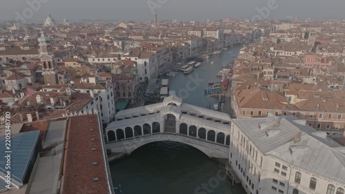 Aerial view of the historic Rialto Bridge spanning the Grand Canal, surrounded by traditional terracotta rooftops and historic buildings in Venice, Veneto, Italy.